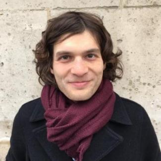 Dr. Jon Forrest standing in front of light brick wall with black coat and burgundy sweater